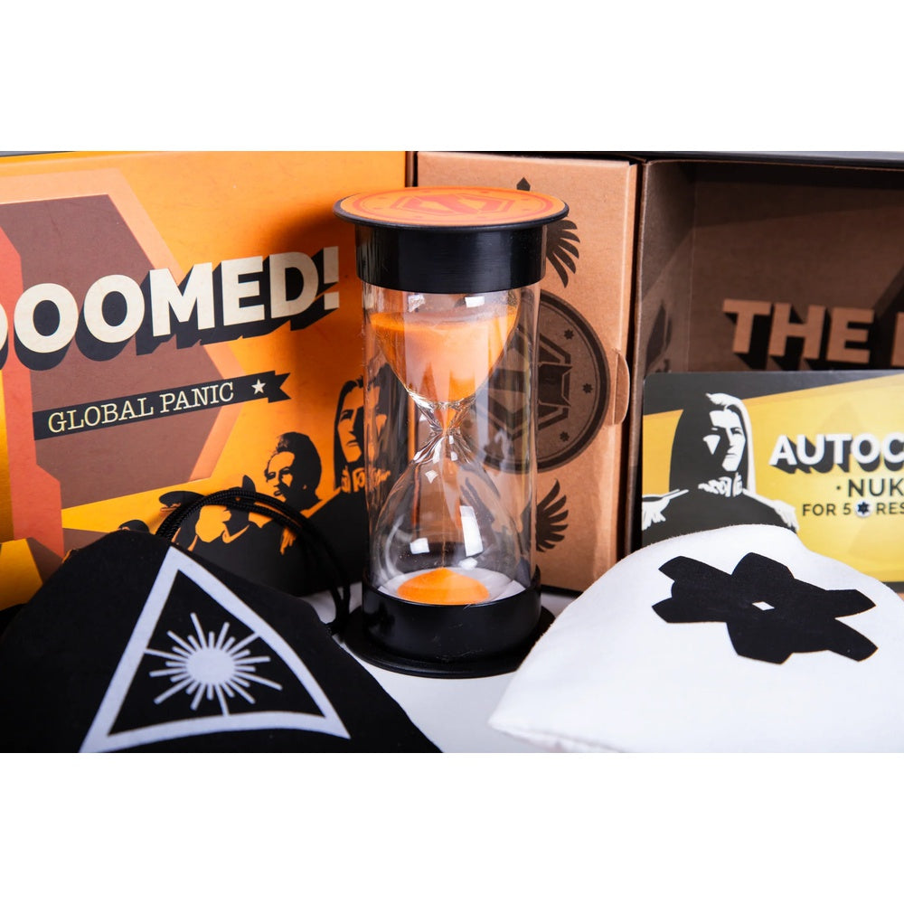 A curated product display featuring a clear glass hourglass with orange sand, surrounded by branded merchandise including a black pouch with a white geometric logo, a white pouch with a black logo, and orange and brown packaging boxes.