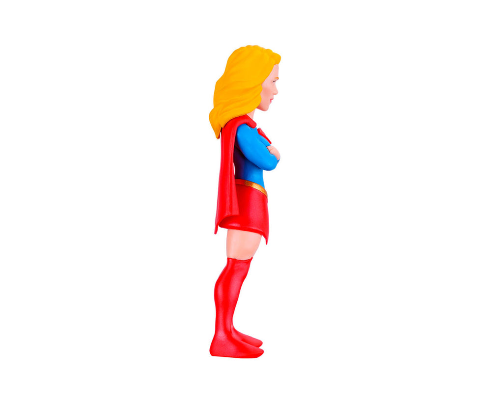 A small plastic toy figurine of a female superhero character shown in side profile, with yellow hair, a blue top, red cape and skirt, and red boots, isolated on a white background.